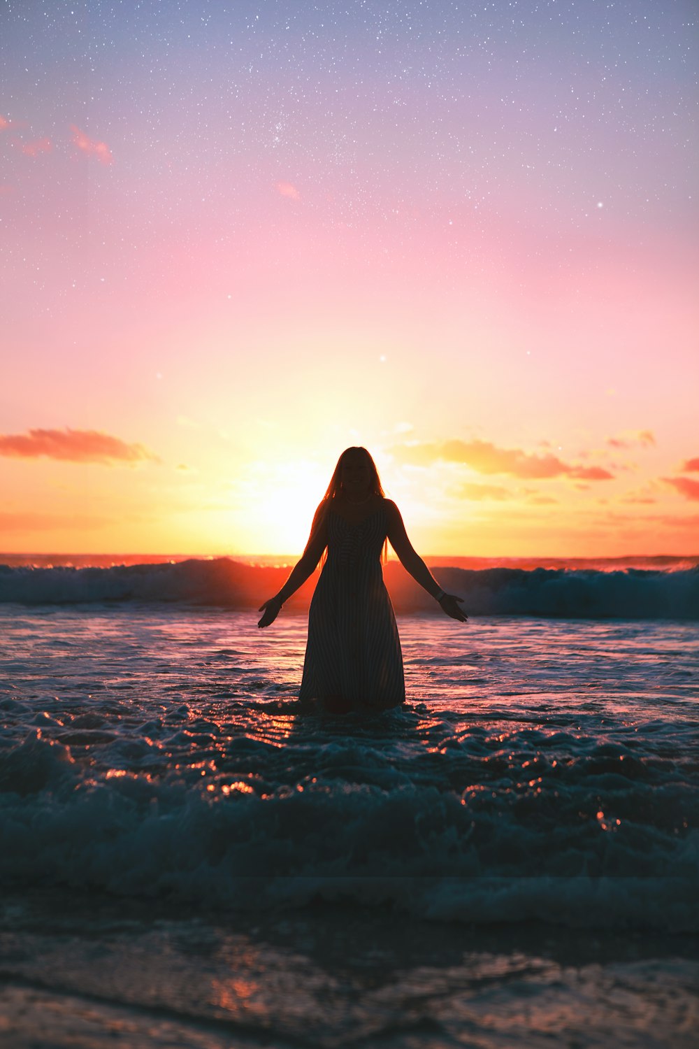 Frau in weißem Kleid steht bei Sonnenuntergang am Meeresufer