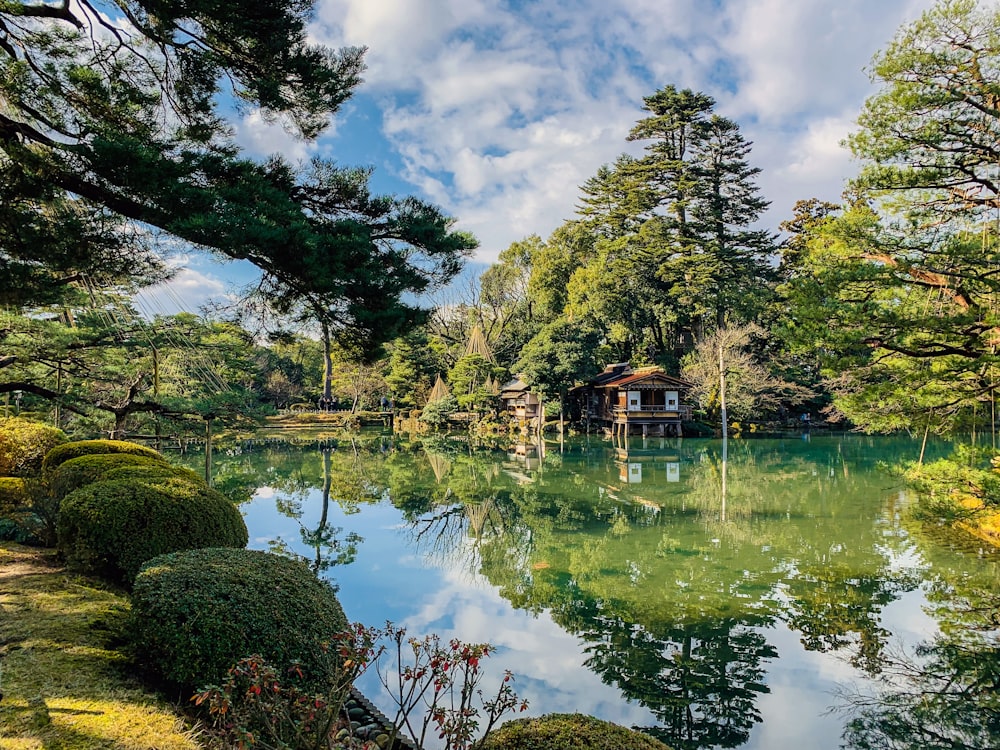 Casa de madera marrón cerca de árboles verdes y lago bajo cielo azul y nubes blancas durante el día