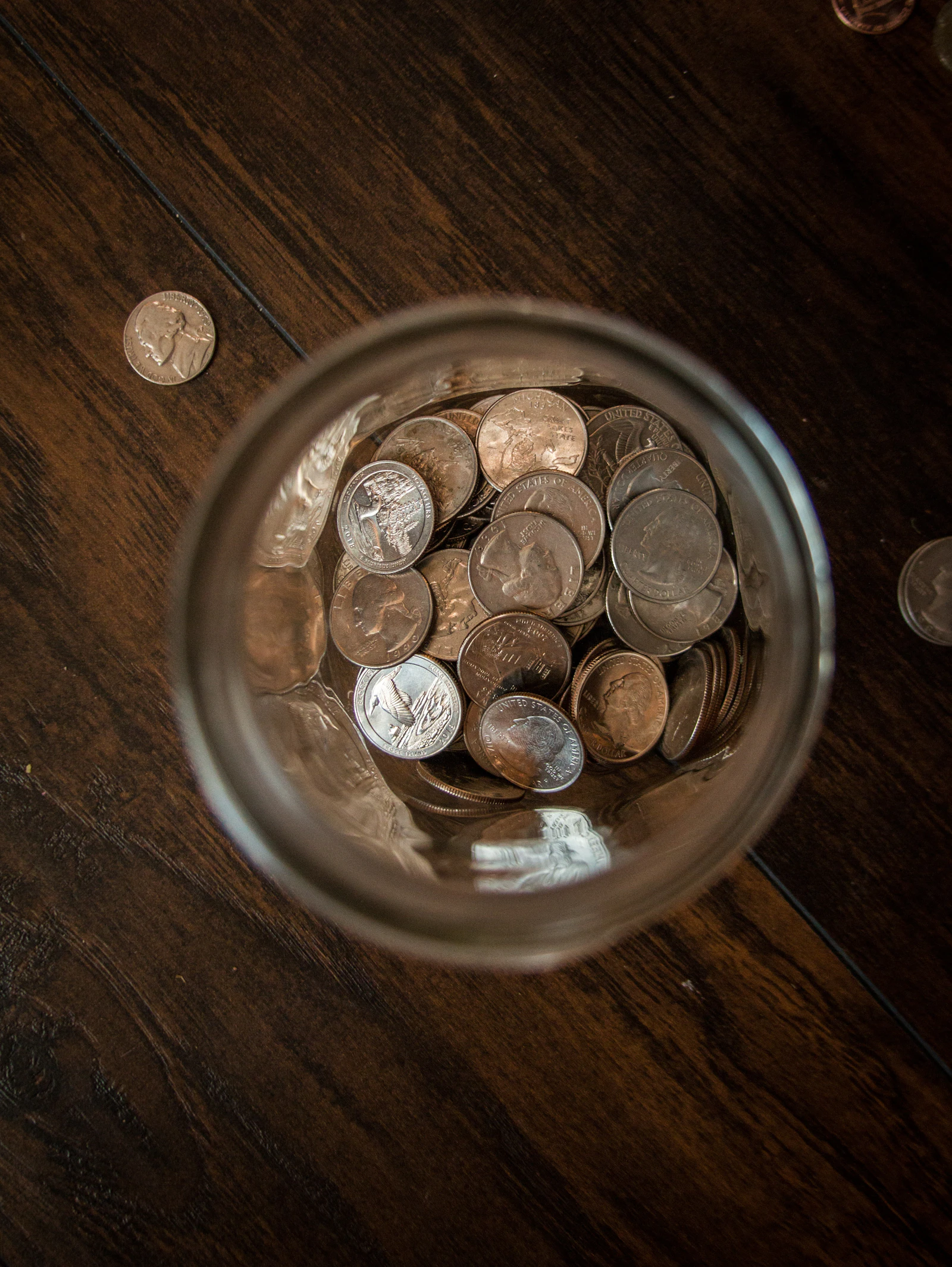Pièces de monnaie rassemblées dans un bocal en verre posé sur une table en bois