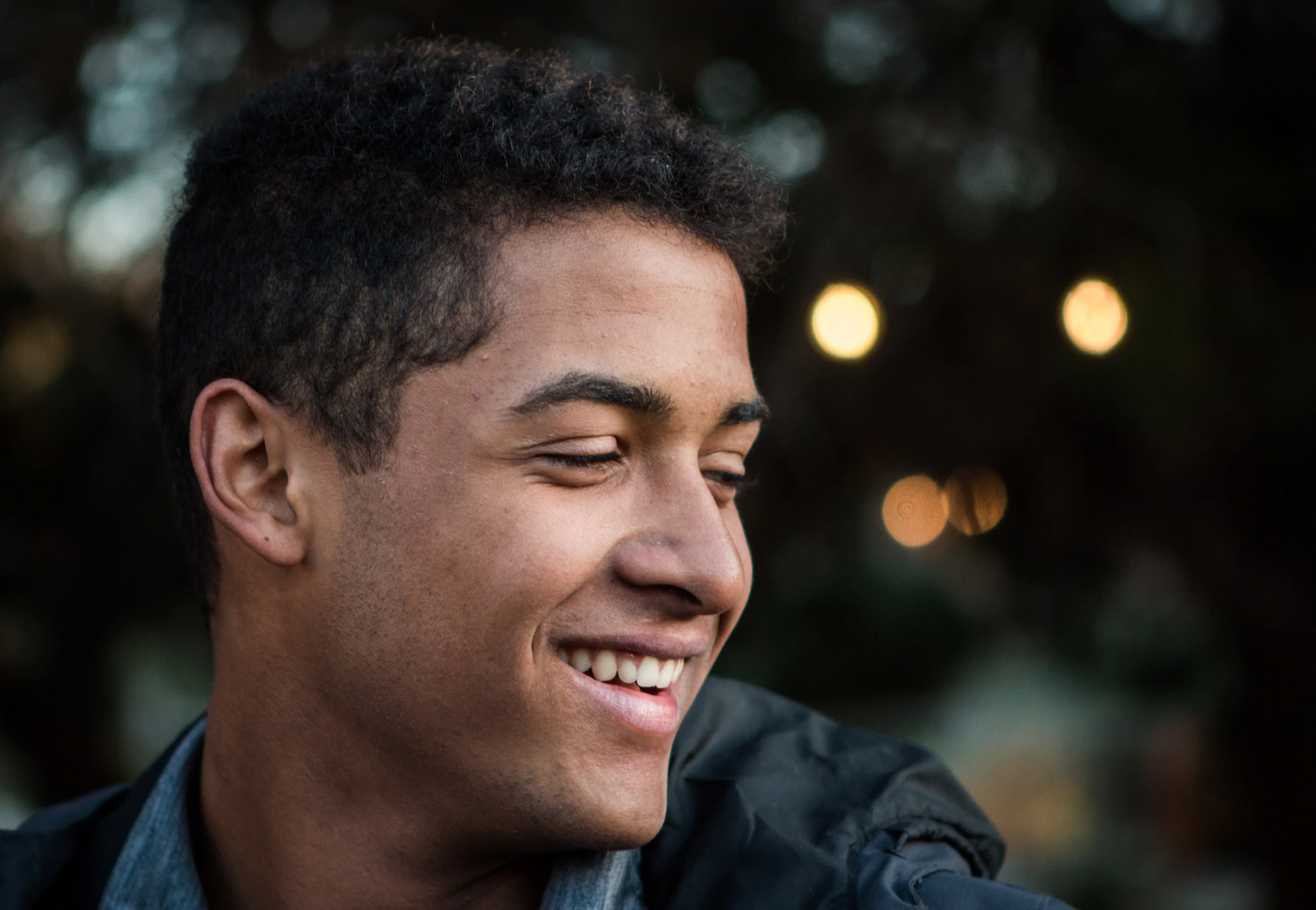 Joven sonriendo al atardecer con luces desenfocadas de fondo