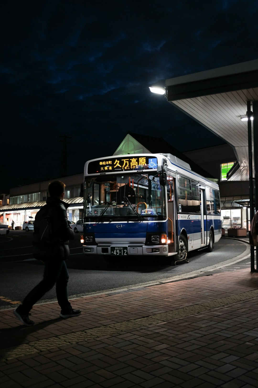 man in black jacket standing near blue bus during night time