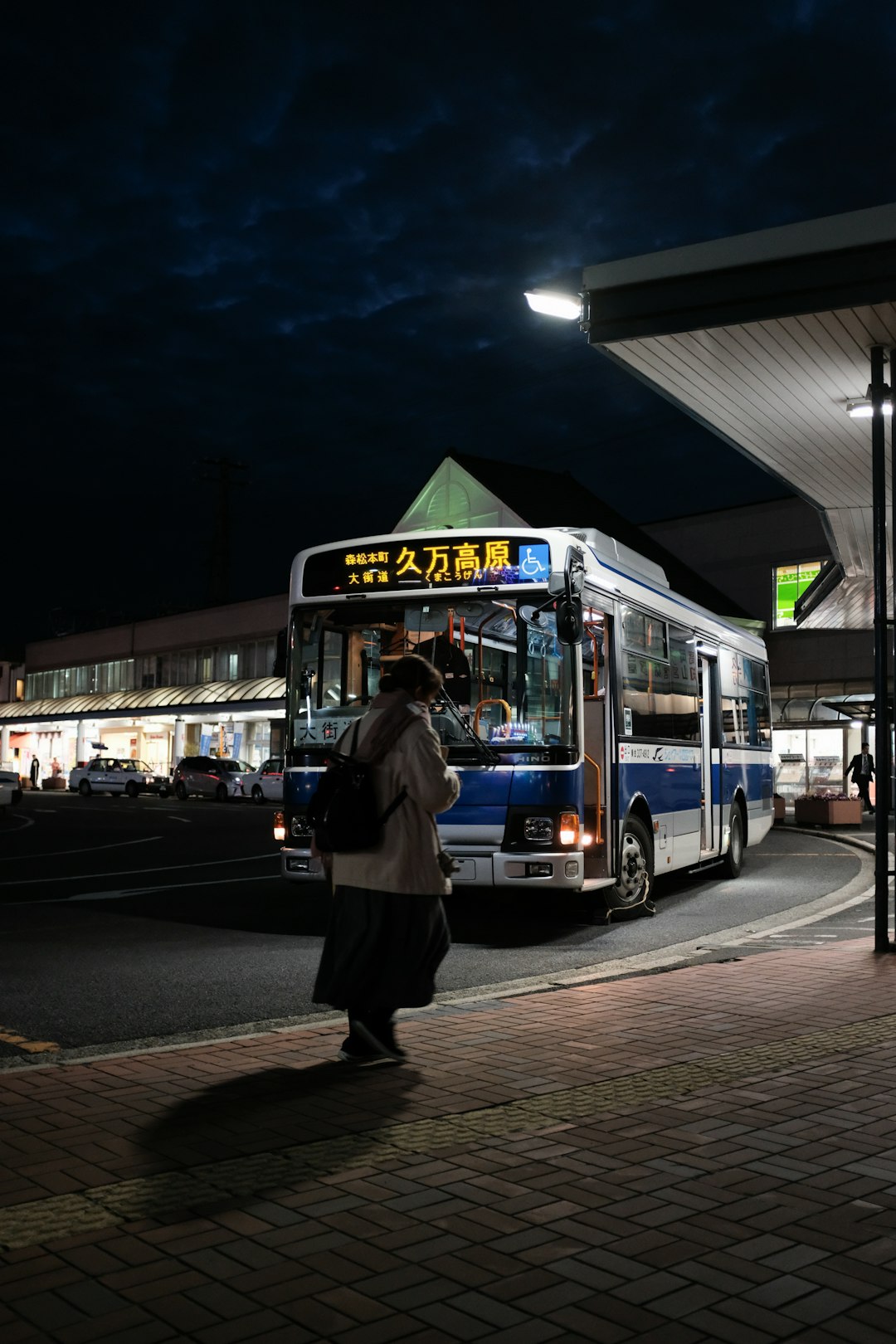 man in black jacket standing near blue bus during night time