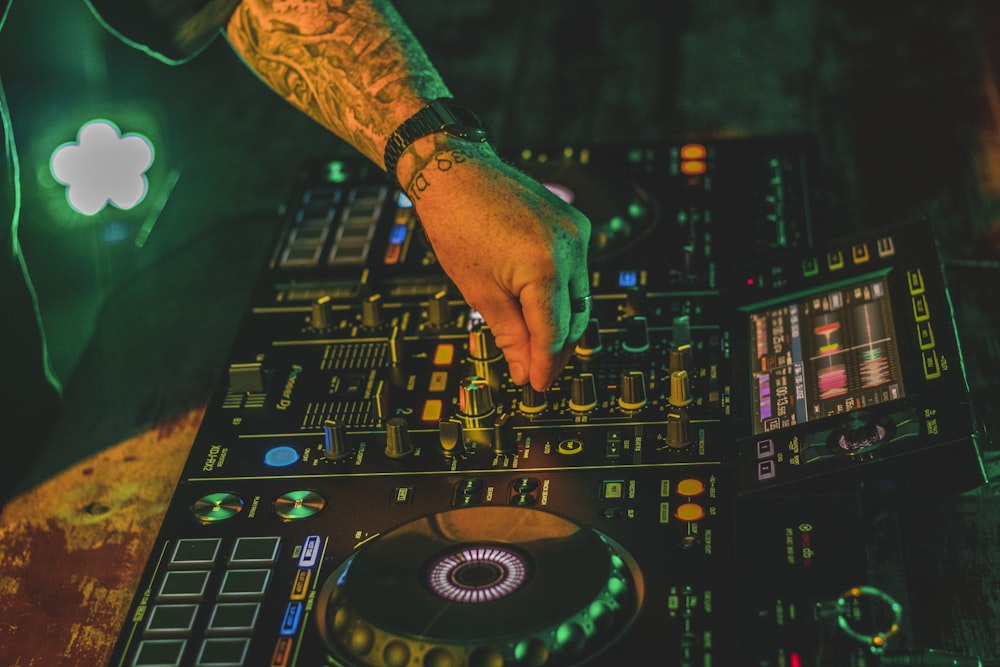 person playing dj mixer with green lights