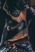 A DJ wearing headphones, focused intensely while adjusting sound levels.
