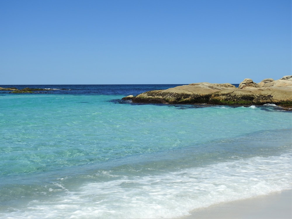 formação rochosa marrom no mar sob o céu azul durante o dia