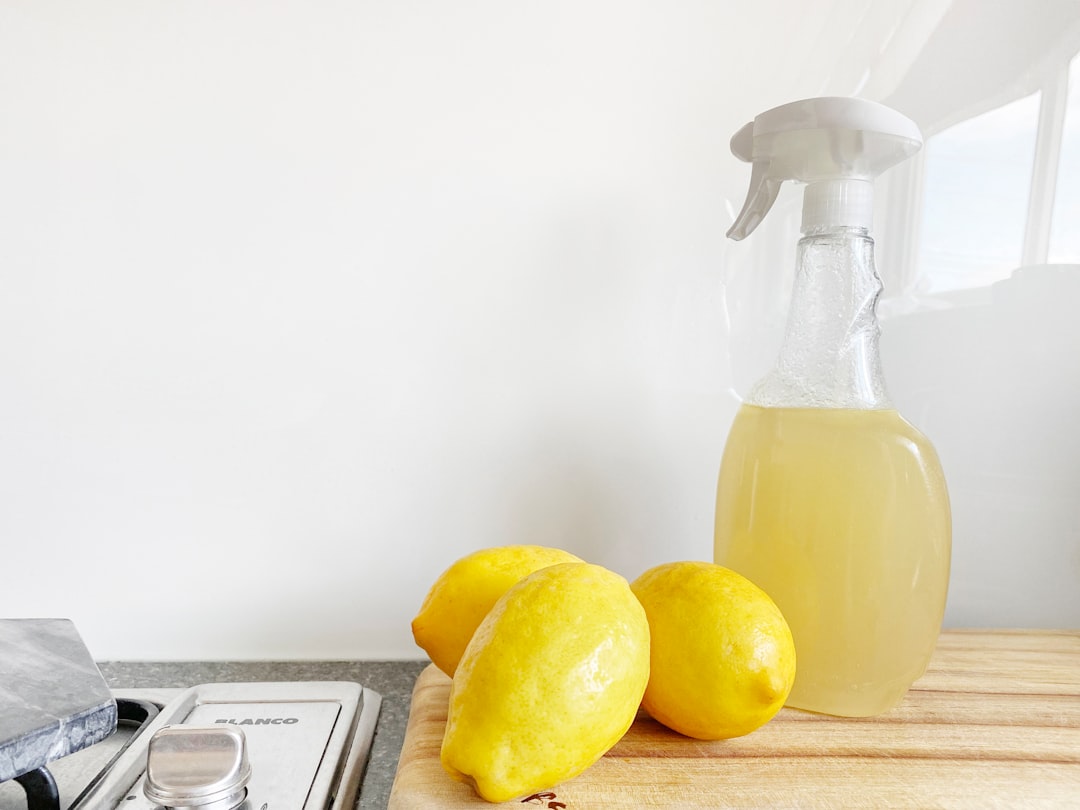 A spray bottle with a yellow liquid next to three lemons on a wooden surface, suggesting natural cleaning products.