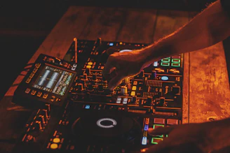 Close-up of hands adjusting DJ mixer knobs with soft silver and electric purple ambient lighting.