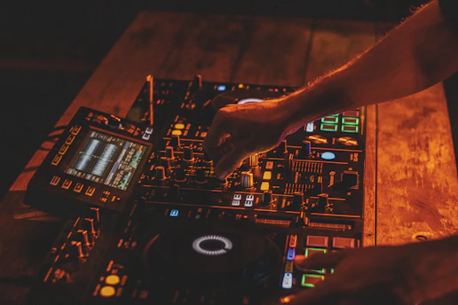 Close-up of hands adjusting DJ mixer knobs with soft silver and electric purple ambient lighting.