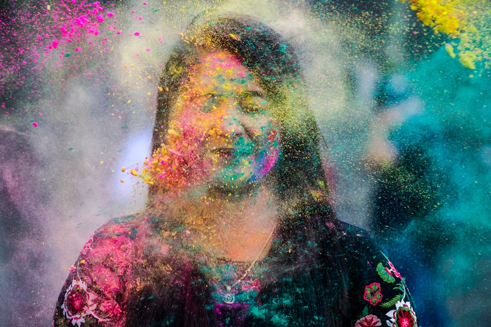 woman in black and red floral shirt with yellow and green powder on her face