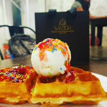 A scoop of ice cream in a waffle cone topped with sprinkles and a cherry.