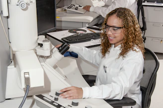 Professional female biochemist in lab coat working with advanced microscope in a clinical laboratory.