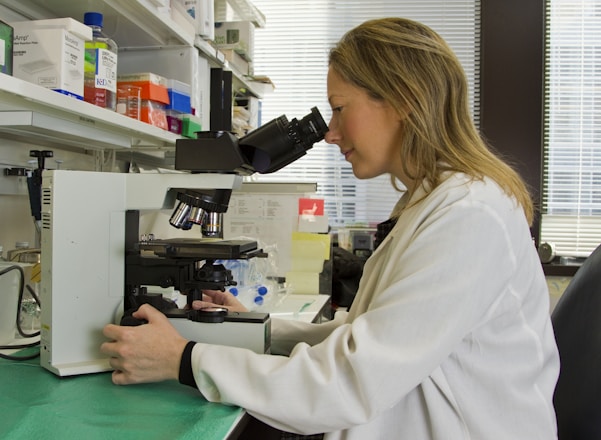 Photograph of a scientist in a lab coat carefully inspecting pharmaceutical samples in a modern laboratory.