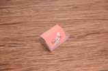 A stack of peach-colored business cards is placed inside a transparent holder on a wooden surface. The cards have a logo with the text 'The Twisted Trio' and a small silhouette of a head profile.