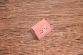 A stack of peach-colored business cards is placed inside a transparent holder on a wooden surface. The cards have a logo with the text 'The Twisted Trio' and a small silhouette of a head profile.