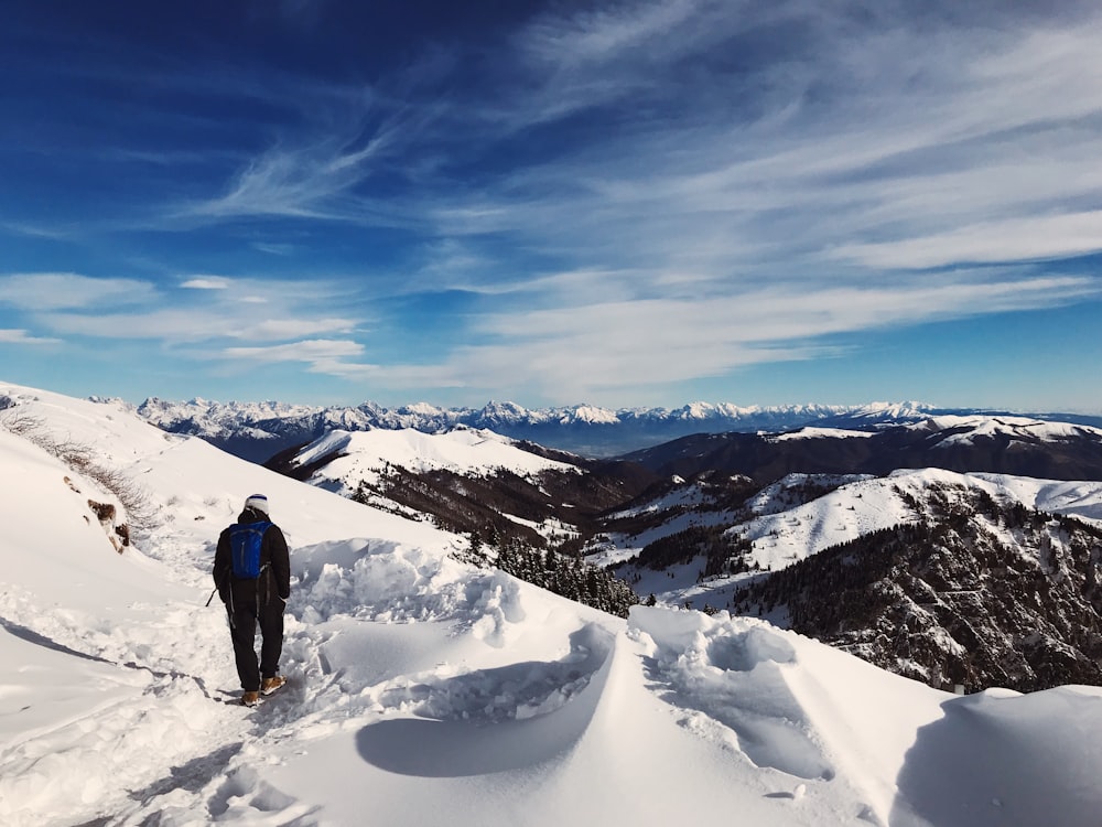 man in blue jacket and black pants standing on snow covered ground during daytime