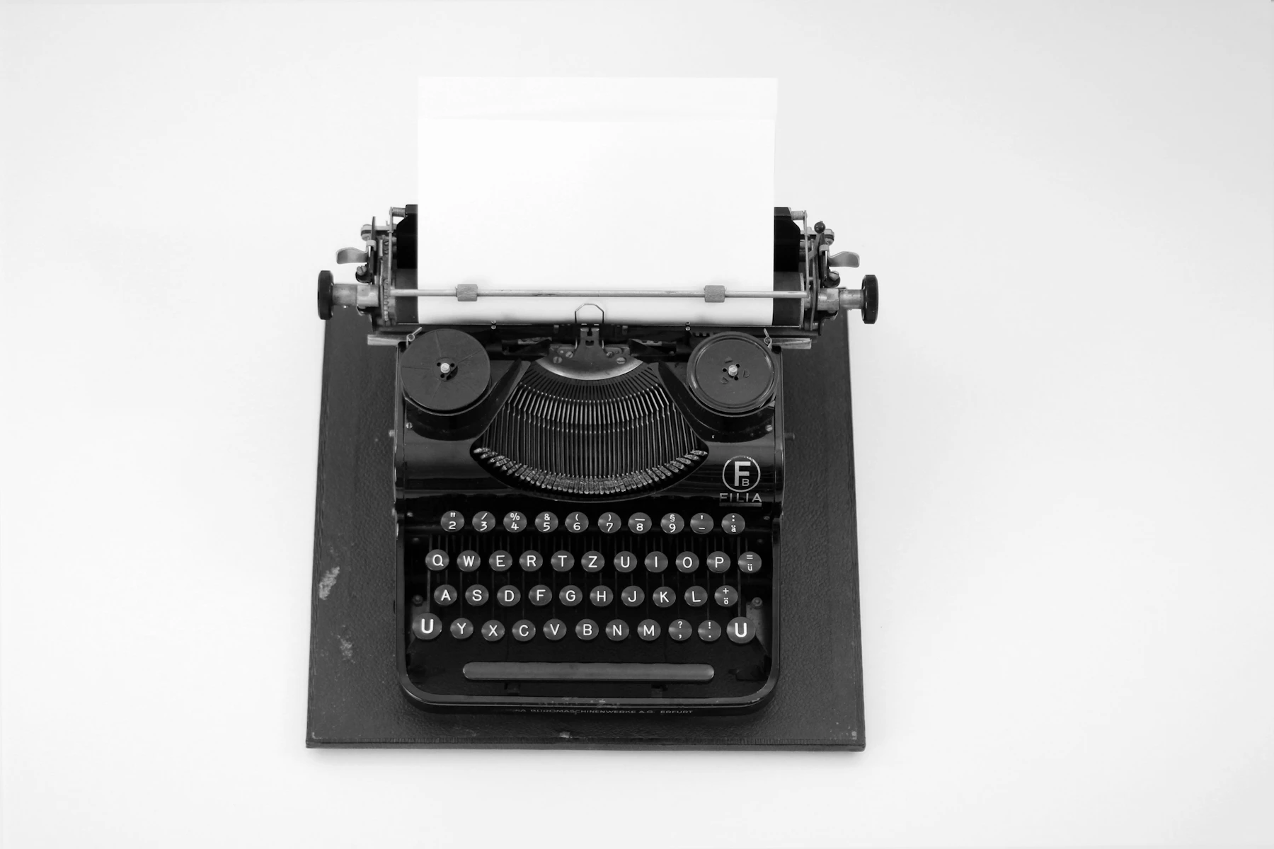 A black manual typewriter with a blank sheet of paper loaded, on a white table