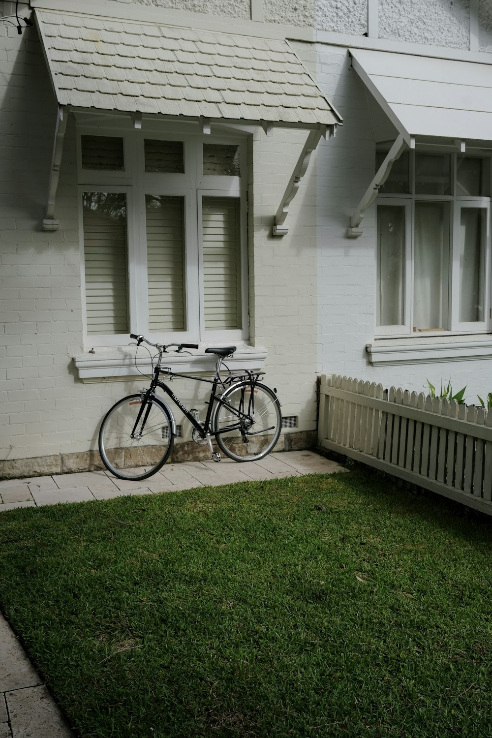 black city bike parked beside white wooden fence