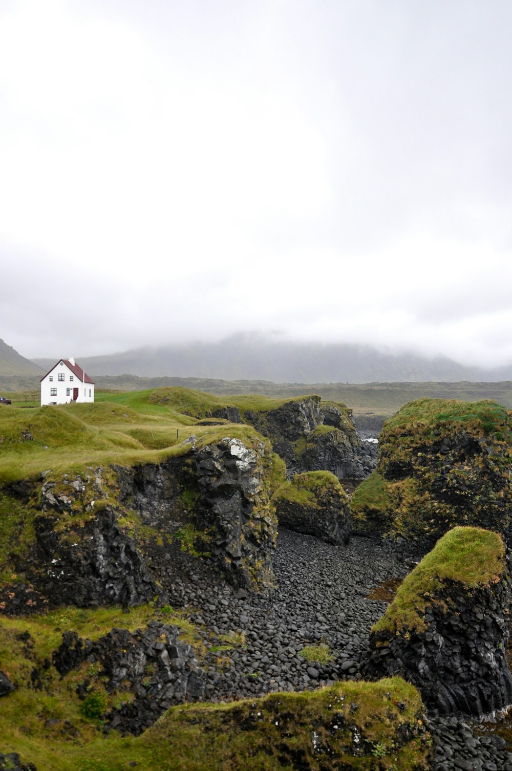 white and red house on green grass covered hill under white cloudy sky during daytime