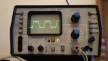 Close-up of a digital oscilloscope displaying waveforms on its screen.