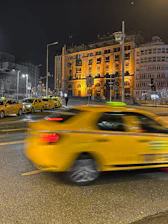 A sleek black and yellow taxi parked in front of a modern building in The Hague at dusk.