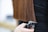 A person with long, straight brown hair is having their hair trimmed with electric clippers. The hair appears healthy and well-maintained, and the person performing the haircut is unseen, holding the clippers near the ends of the hair.