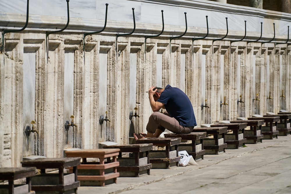 man in blue t-shirt sitting on brown wooden bench during daytime