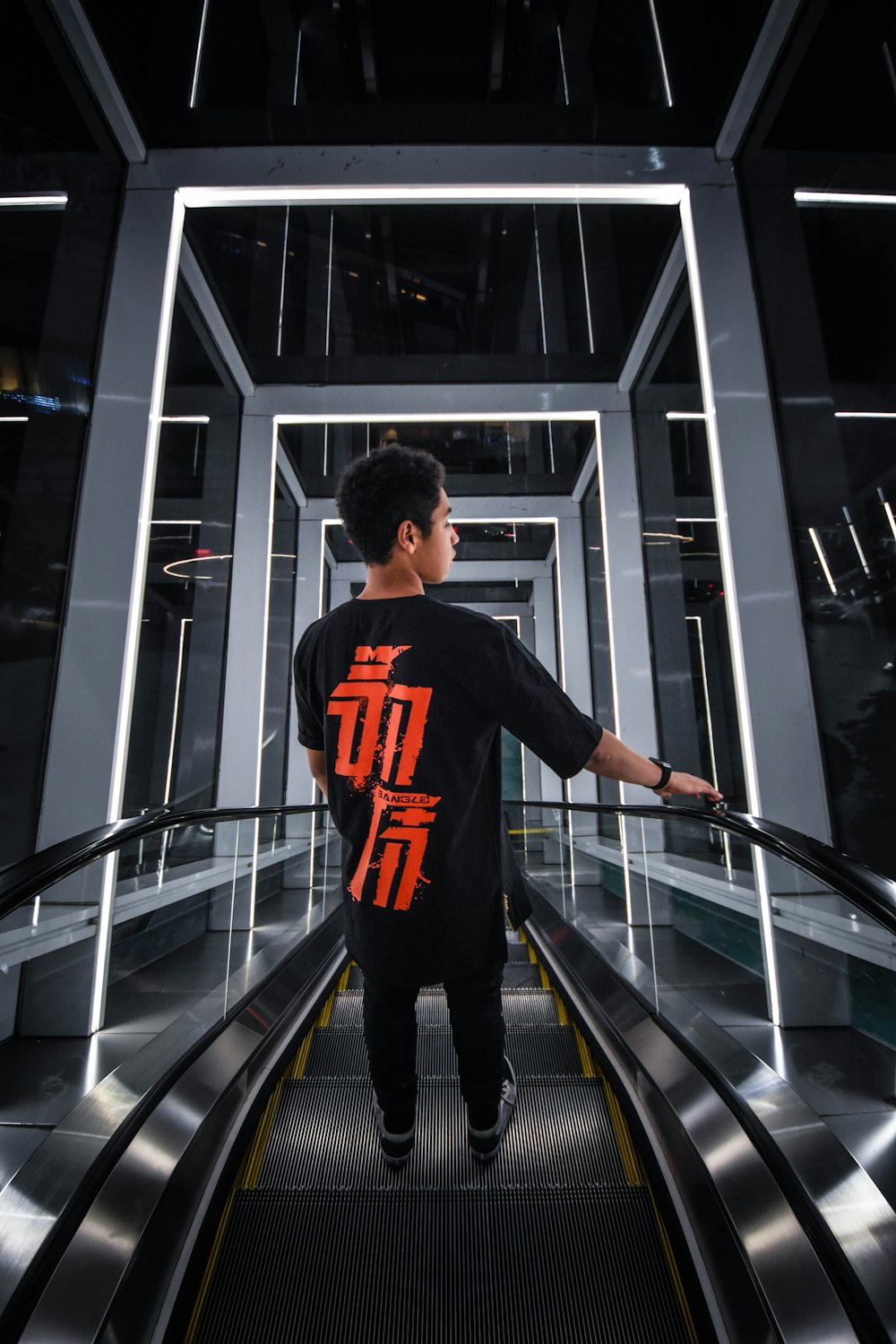man in black and orange nike crew neck t-shirt and black pants standing on escalator
