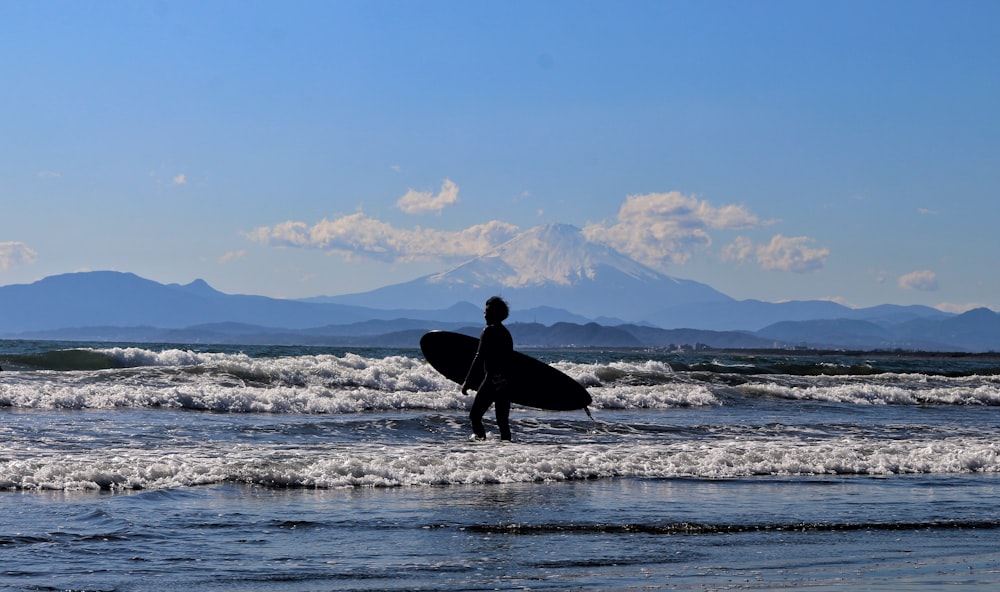 hombre con chaqueta y pantalones negros sosteniendo la tabla de surf caminando en la orilla del mar durante el día