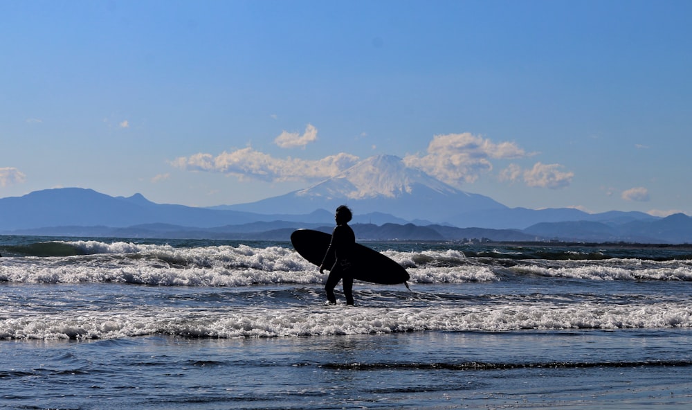 uomo in giacca e pantaloni neri che tengono la tavola da surf che cammina in riva al mare durante il giorno