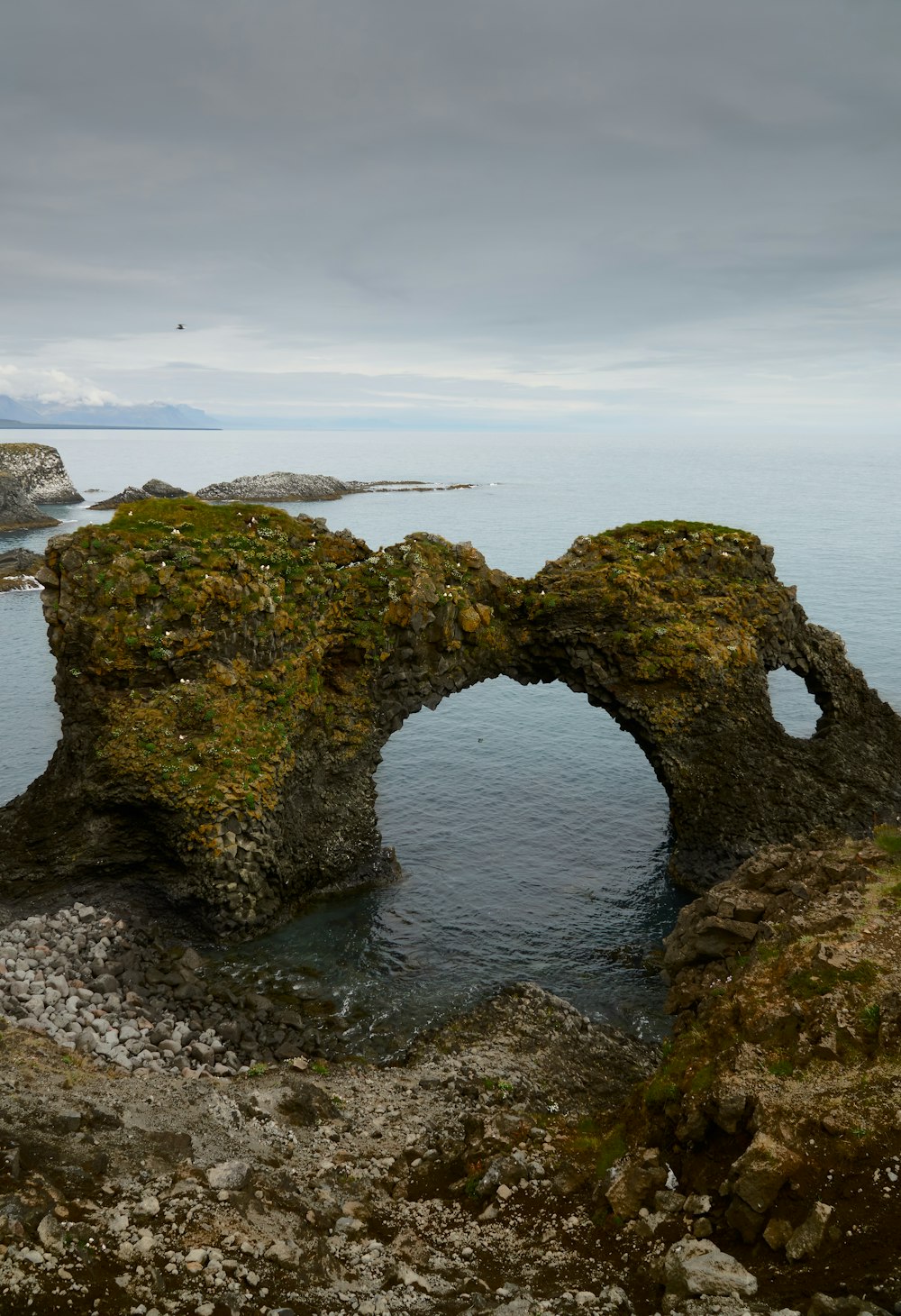 green moss covered rock formation on sea under white clouds during daytime