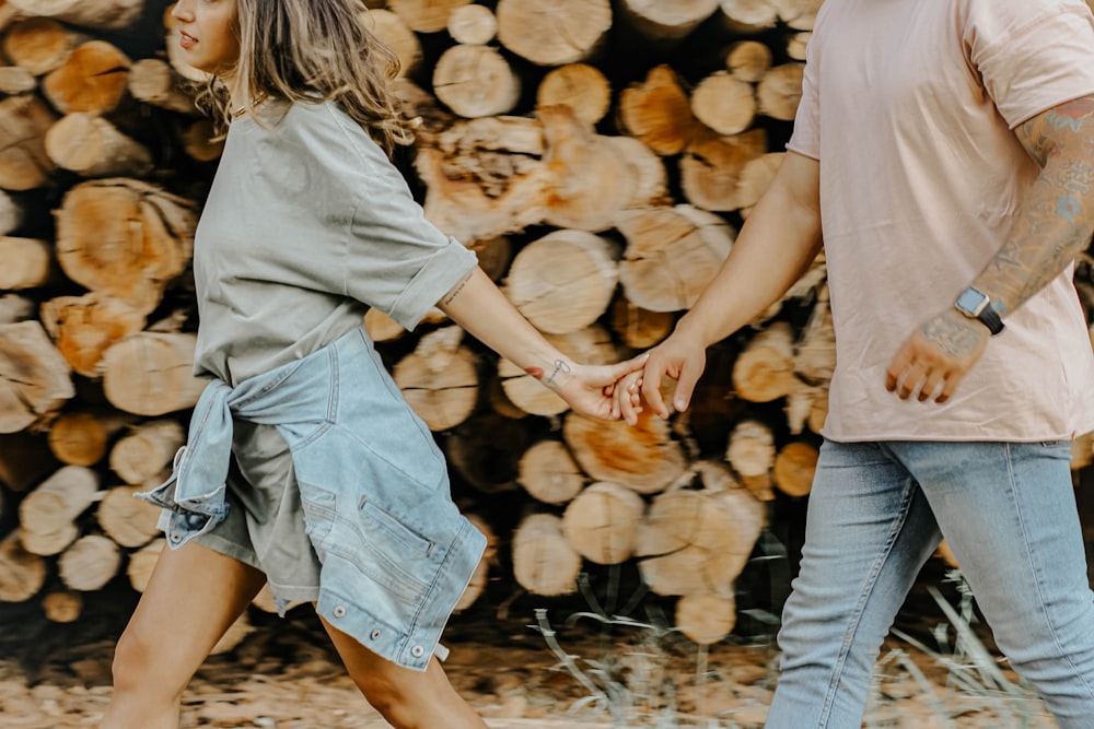 man and woman holding hands while walking on dried leaves