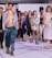 A diverse group of models walks confidently down a runway, showcasing a variety of fashion styles including metallic and patterned fabrics. The setting is a fashion show, and the models display an array of outfits ranging from casual to formal wear. Their expressions are serious and focused, reflecting the professional atmosphere of the event.