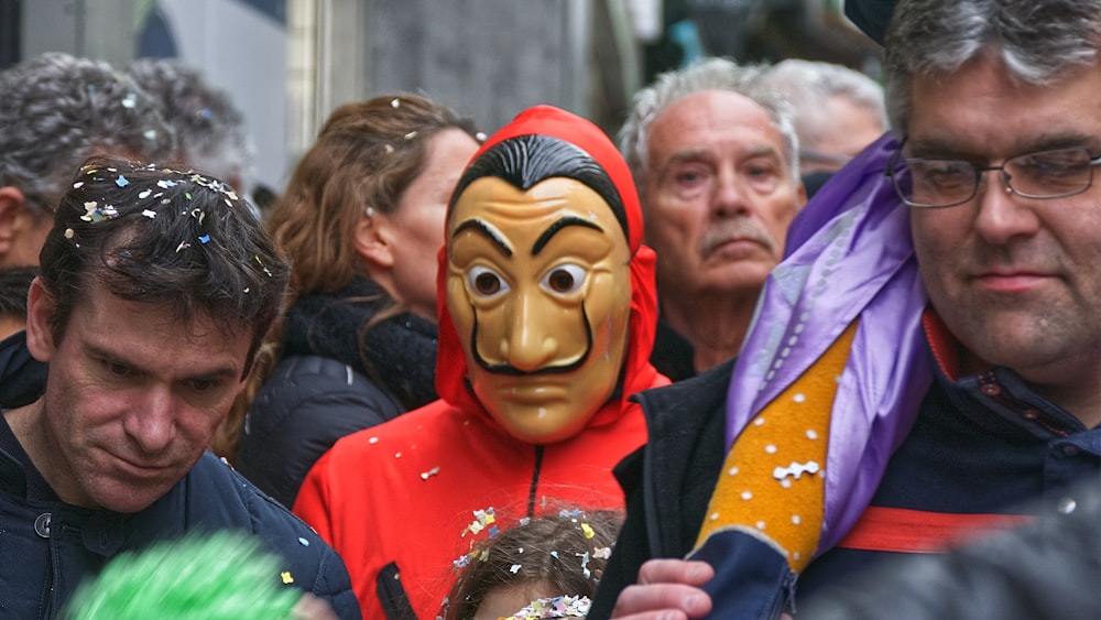 a group of people standing around a man wearing a mask