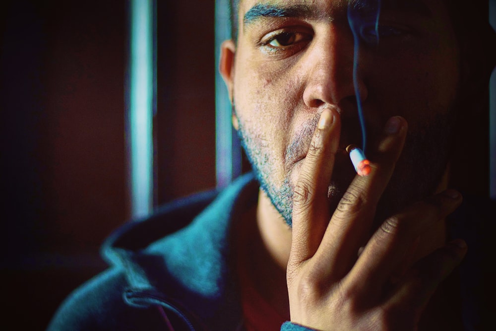 hombre con camisa azul de cuello redondo sosteniendo un palo de cigarrillo