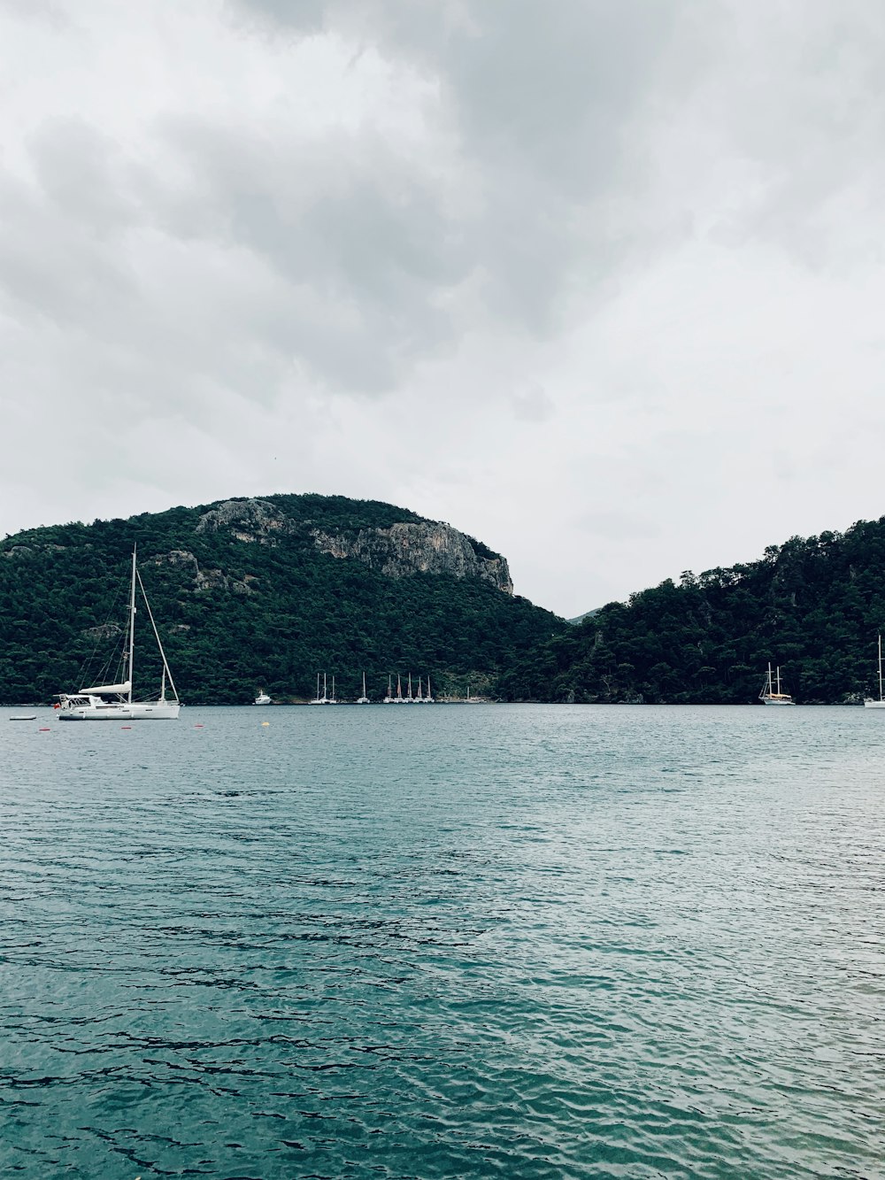 white boat on body of water near green mountain under cloudy sky during daytime