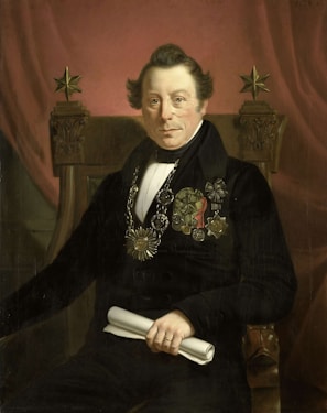 A portrait of a distinguished man seated on an ornate chair, wearing formal attire with various medals and decorations on his chest. He holds a rolled document in one hand and sits against a backdrop of a rich, red curtain. The chair features decorative elements, including two five-pointed stars at the top.