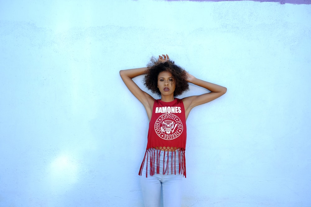 woman in red tank top and white pants standing beside white wall