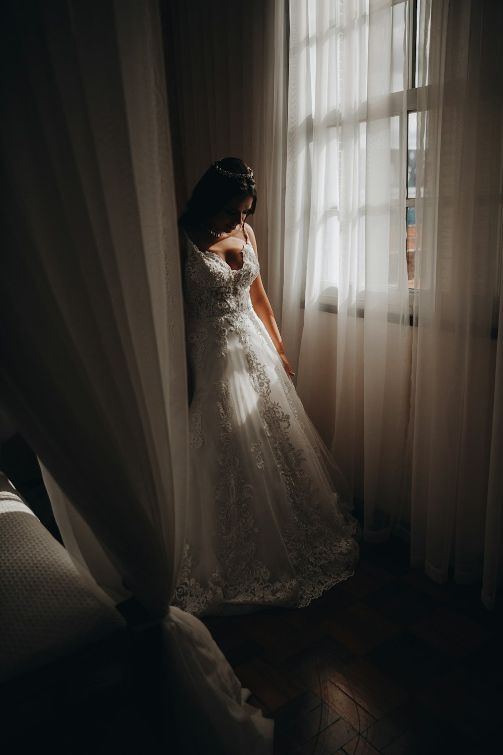 woman in white wedding dress standing beside white window curtain