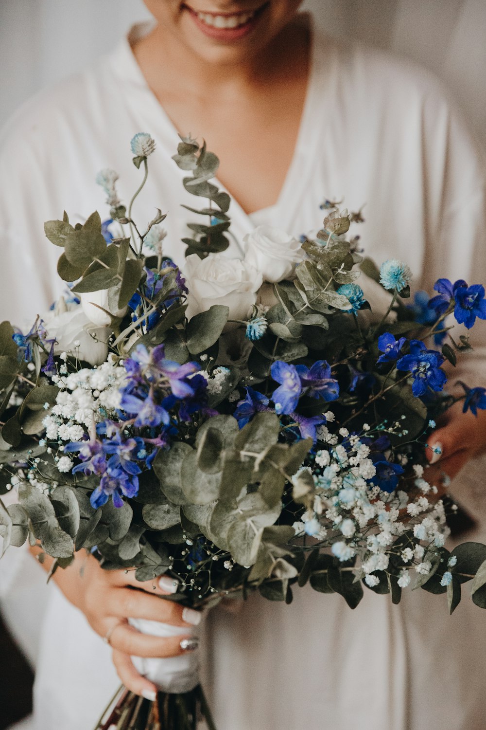 woman in white floral lace wedding dress holding blue and white flowers