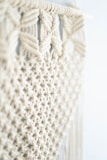 Intricate macramé pattern featuring woven and knotted cord designs, creating a textured and airy appearance. The focus is on the detailed craftsmanship of the knots against a soft, neutral background.
