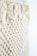 Intricate macramé pattern featuring woven and knotted cord designs, creating a textured and airy appearance. The focus is on the detailed craftsmanship of the knots against a soft, neutral background.