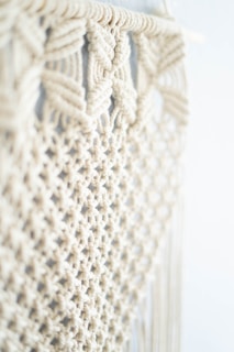 Intricate macram&eacute; pattern featuring woven and knotted cord designs, creating a textured and airy appearance. The focus is on the detailed craftsmanship of the knots against a soft, neutral background.