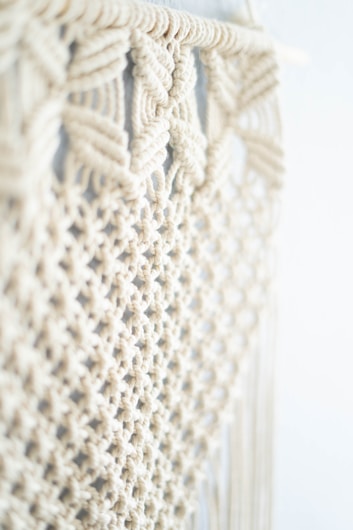 Intricate macram&eacute; pattern featuring woven and knotted cord designs, creating a textured and airy appearance. The focus is on the detailed craftsmanship of the knots against a soft, neutral background.