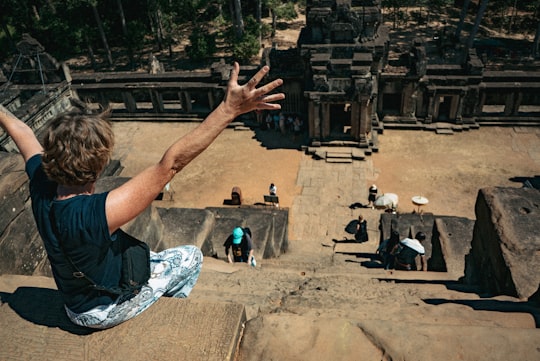man in black t-shirt and blue denim jeans sitting on brown rock formation during daytime in Angkor Wat Cambodia