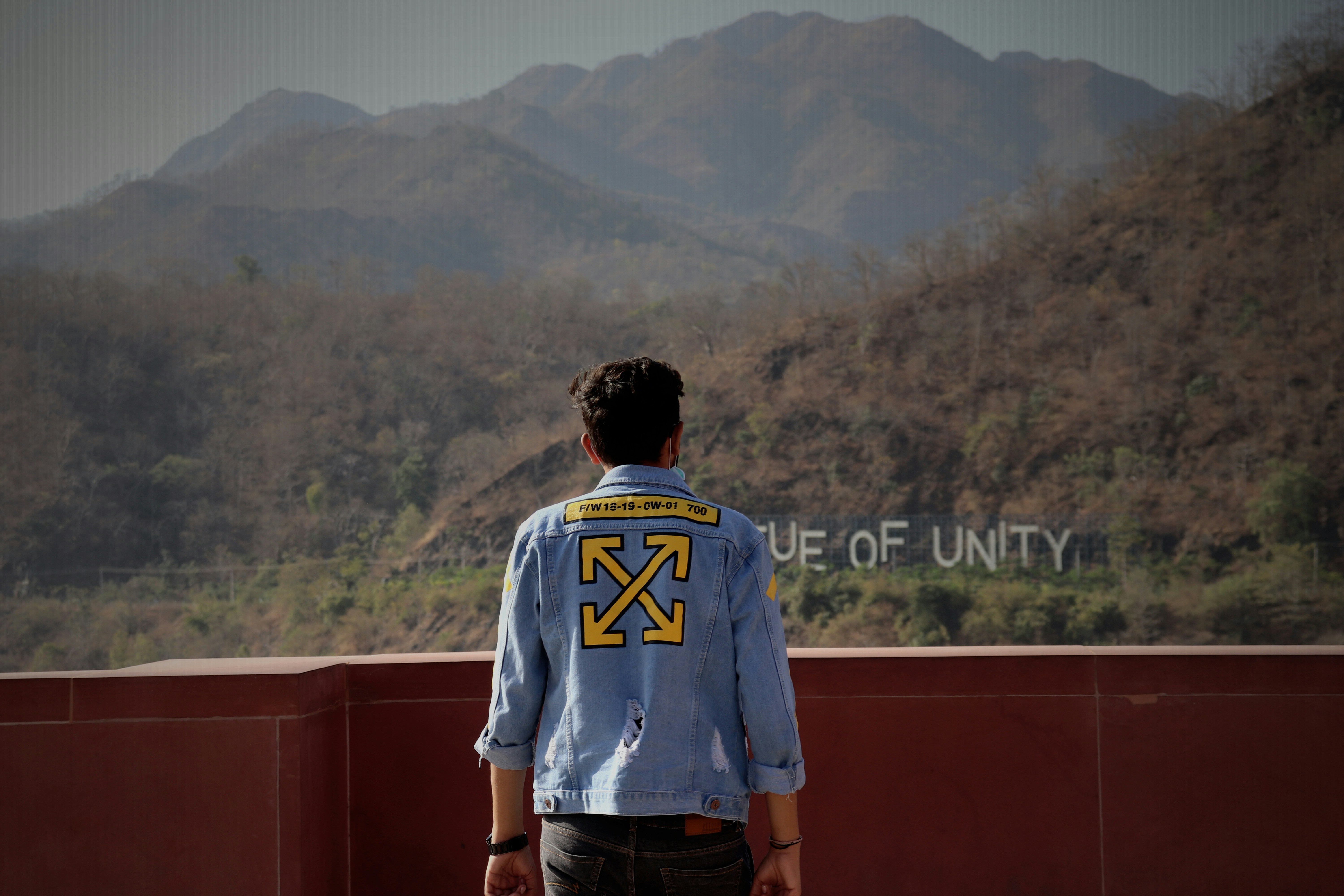 man in white and blue crew neck t-shirt standing on brown concrete wall during daytime