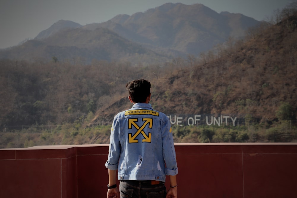 man in white and blue crew neck t-shirt standing on brown concrete wall during daytime