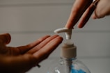 Hand pressing pump dispenser releasing creamy white liquid soap into palm.