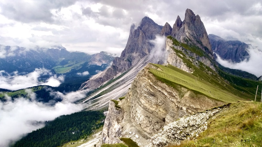 green grass on gray rocky mountain under white cloudy sky during daytime