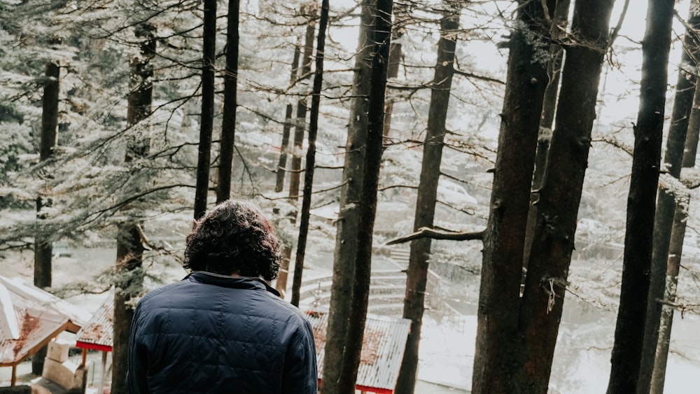 man in blue jacket standing in front of brown trees during daytime