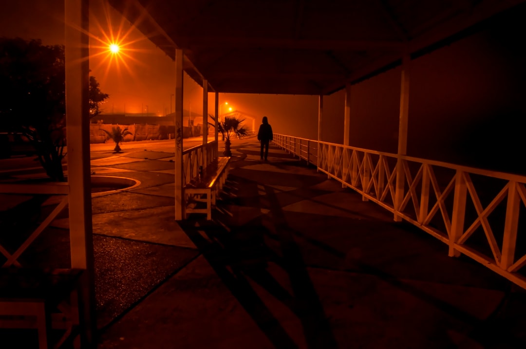 silhouette of man walking on wooden bridge during sunset